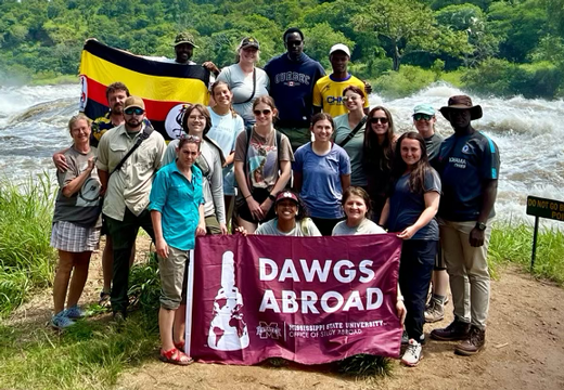 A group of students in Uganda holding a flag that reads dawgs abroad