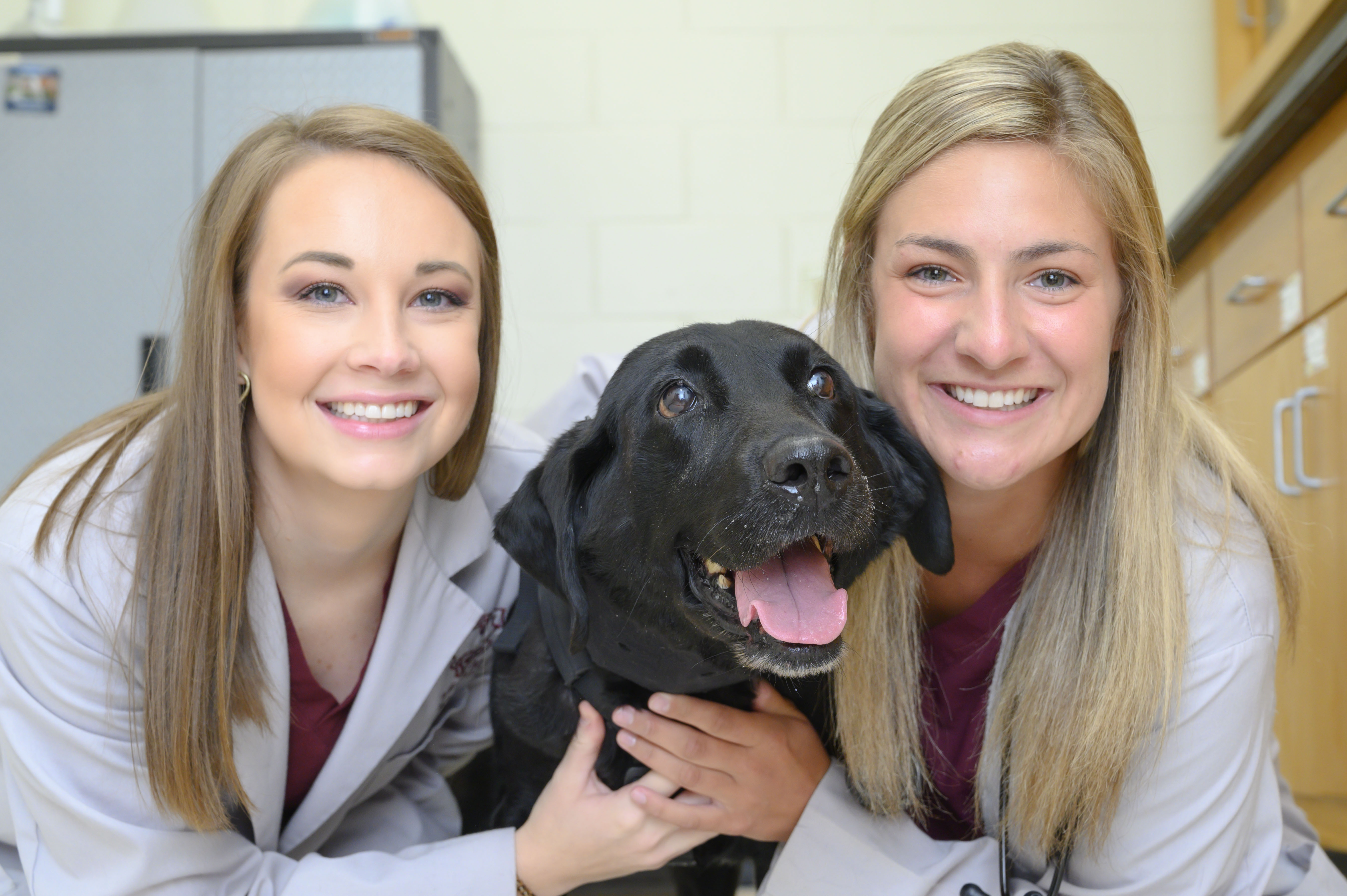 Two students pose with a black Labrador retriever