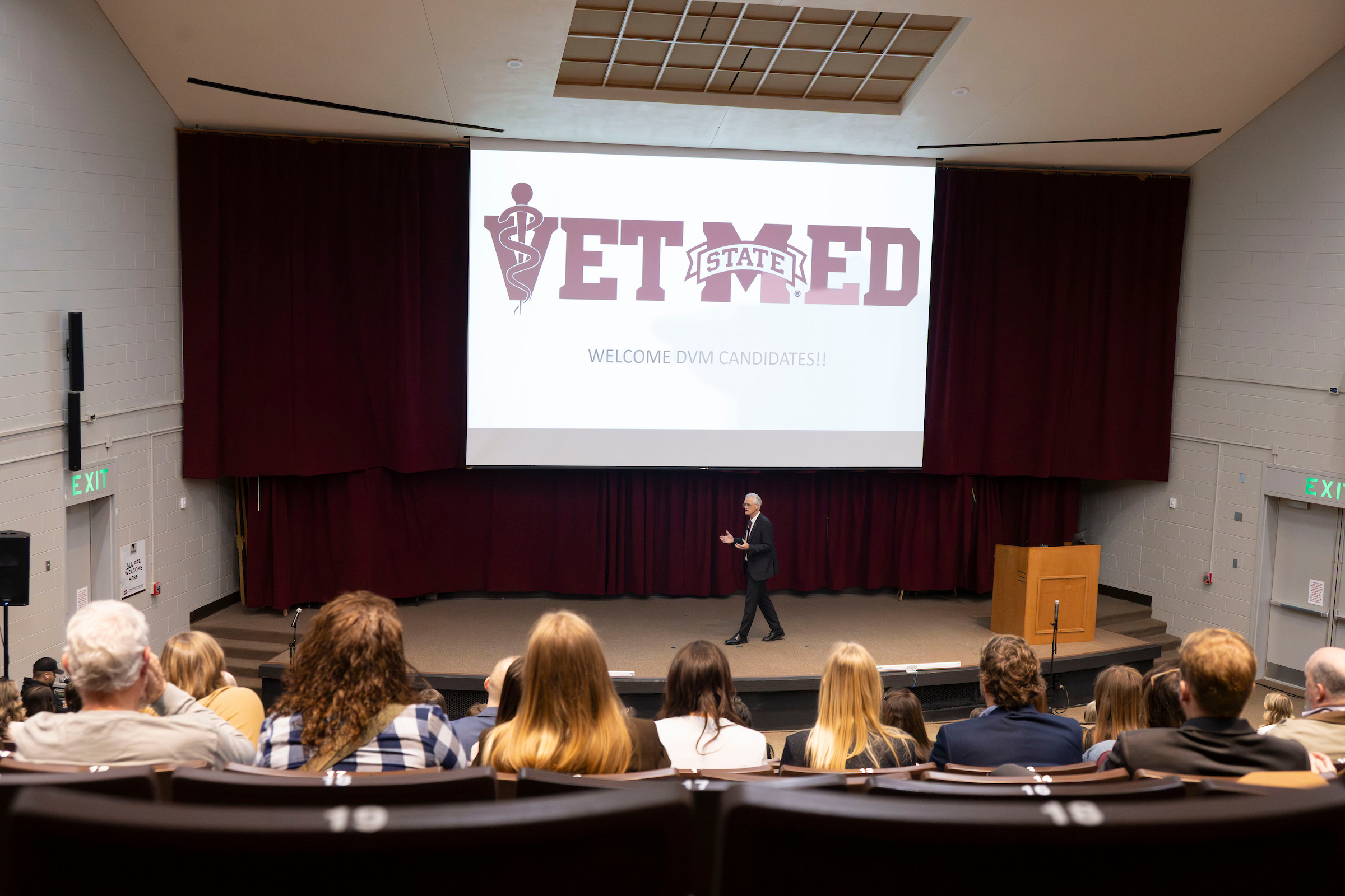 Dr. Nicholas Frank addresses an auditorium filled with people. A screen displays the Vet Med logo.