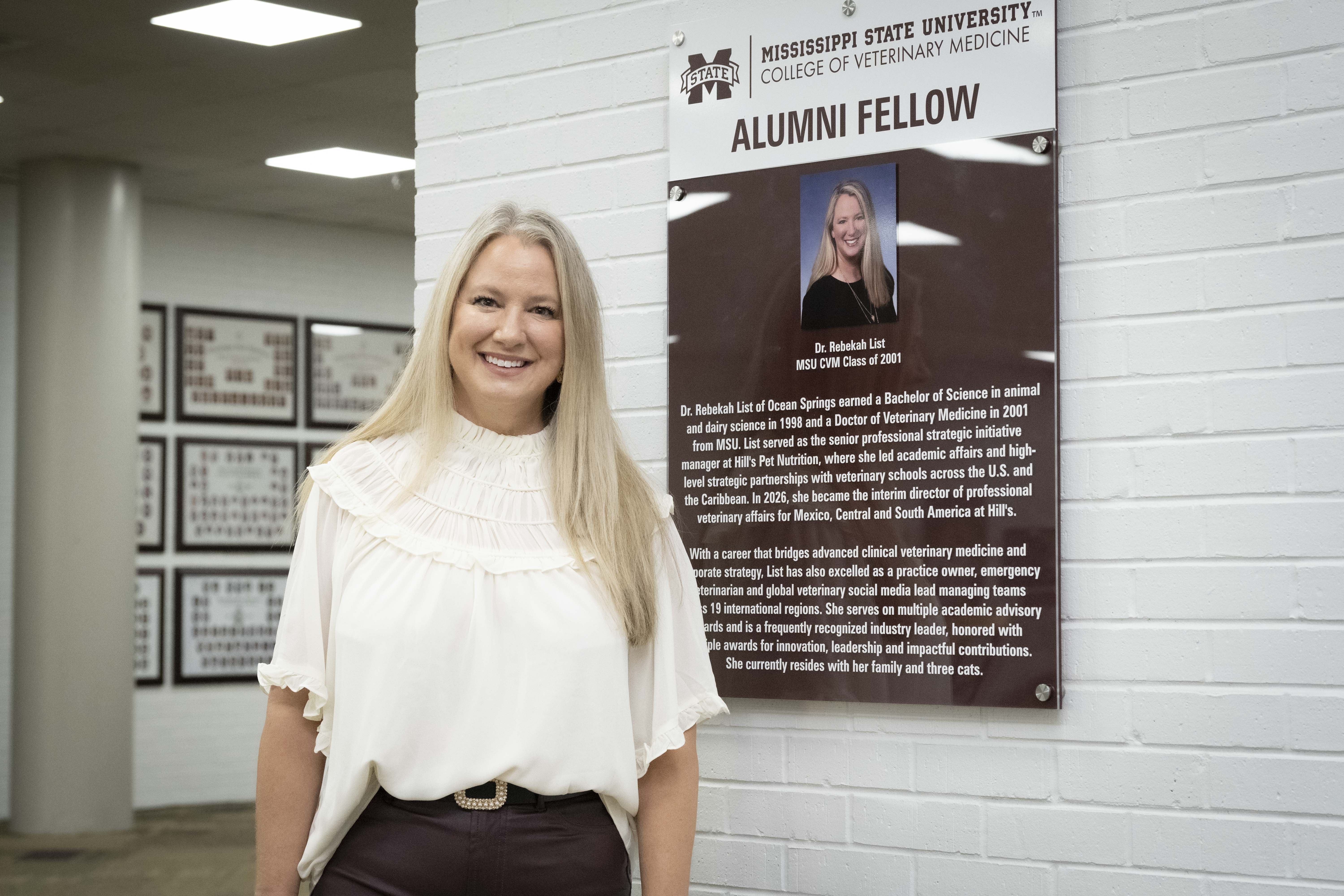 Dr. Rebekah List stands in front of her Alumni Fellow display sign on the second floor of the MSU CVM Wise Center.