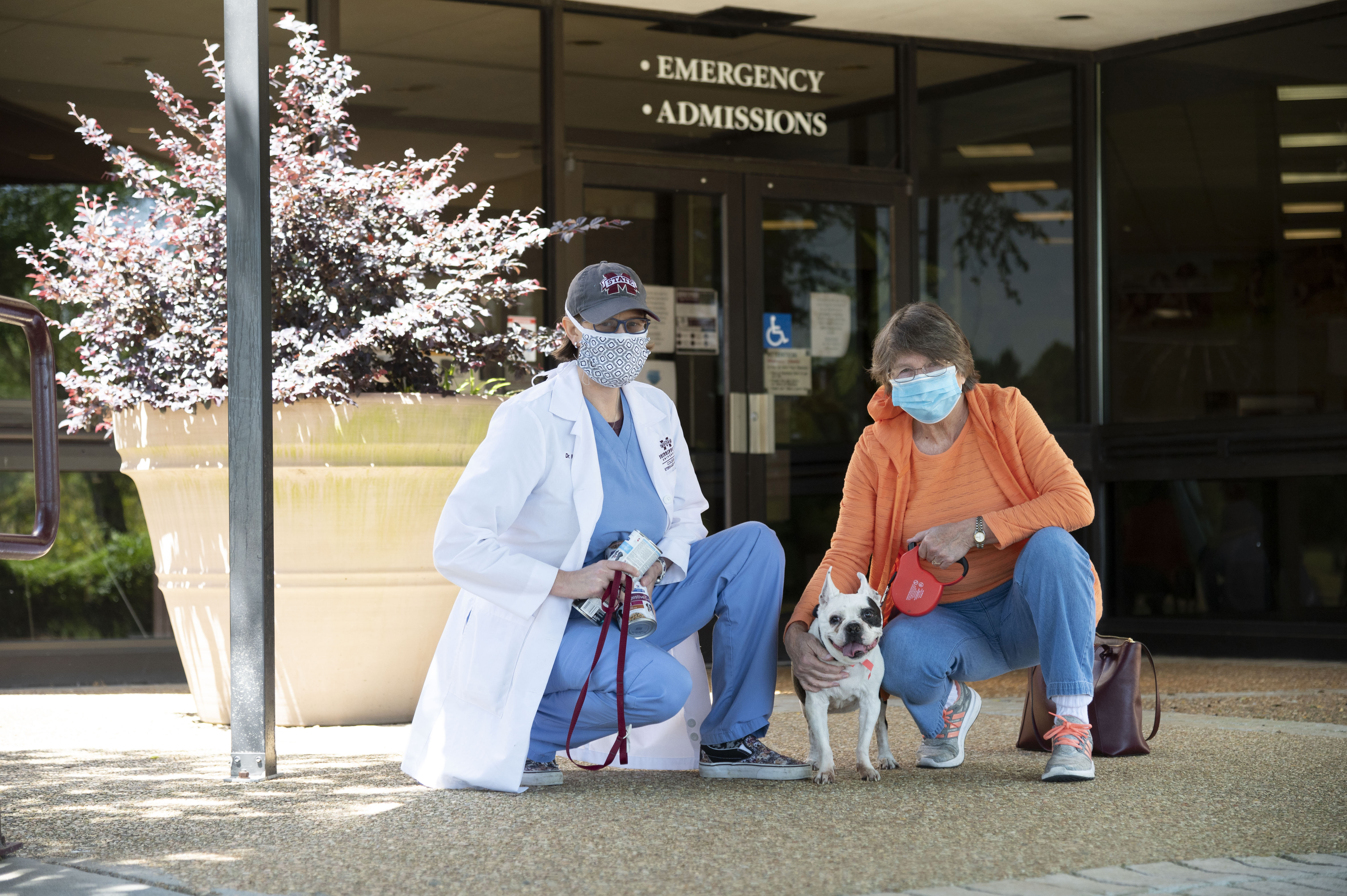 A veterinarian and client pose with masks on holding the patient