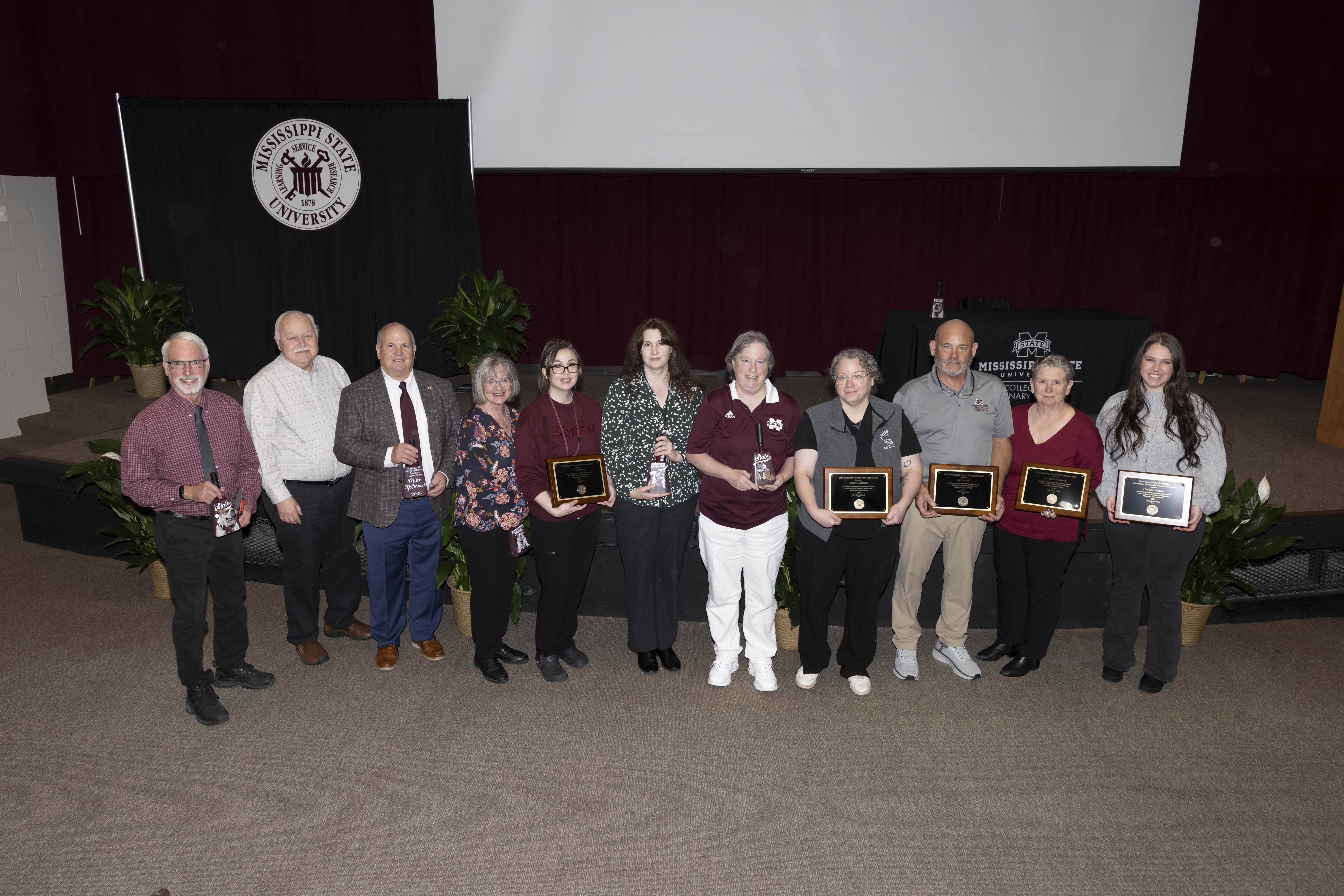 MSU CVM award-winners stand in front of the stage inside the Wise Center auditorium after receiving their awards. From left to right: Dr. Larry Hanson; Dr. Sherman "Skip" Jack; Mike McCormick; Dr. Lora Petrie-Hanson; Katie Bennett; Dr. Brittany Baughman; Terri Snead, CVT; Emily Childers, CVT; Lin Newell; Dr. Pauline Prince; Chelsea Jackson, CVT.