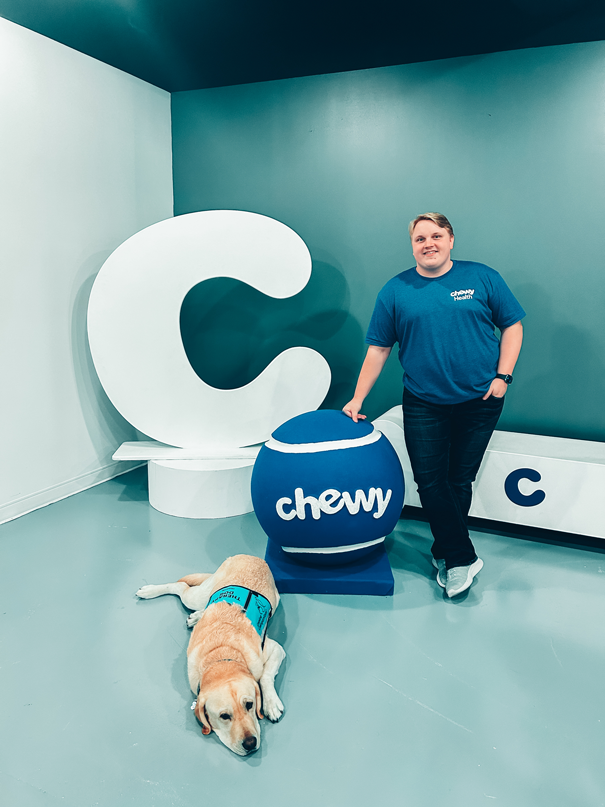 Casey Lavender and a dog. Casey is standing next to a very large tennis ball with the word "Chewy" written on it.