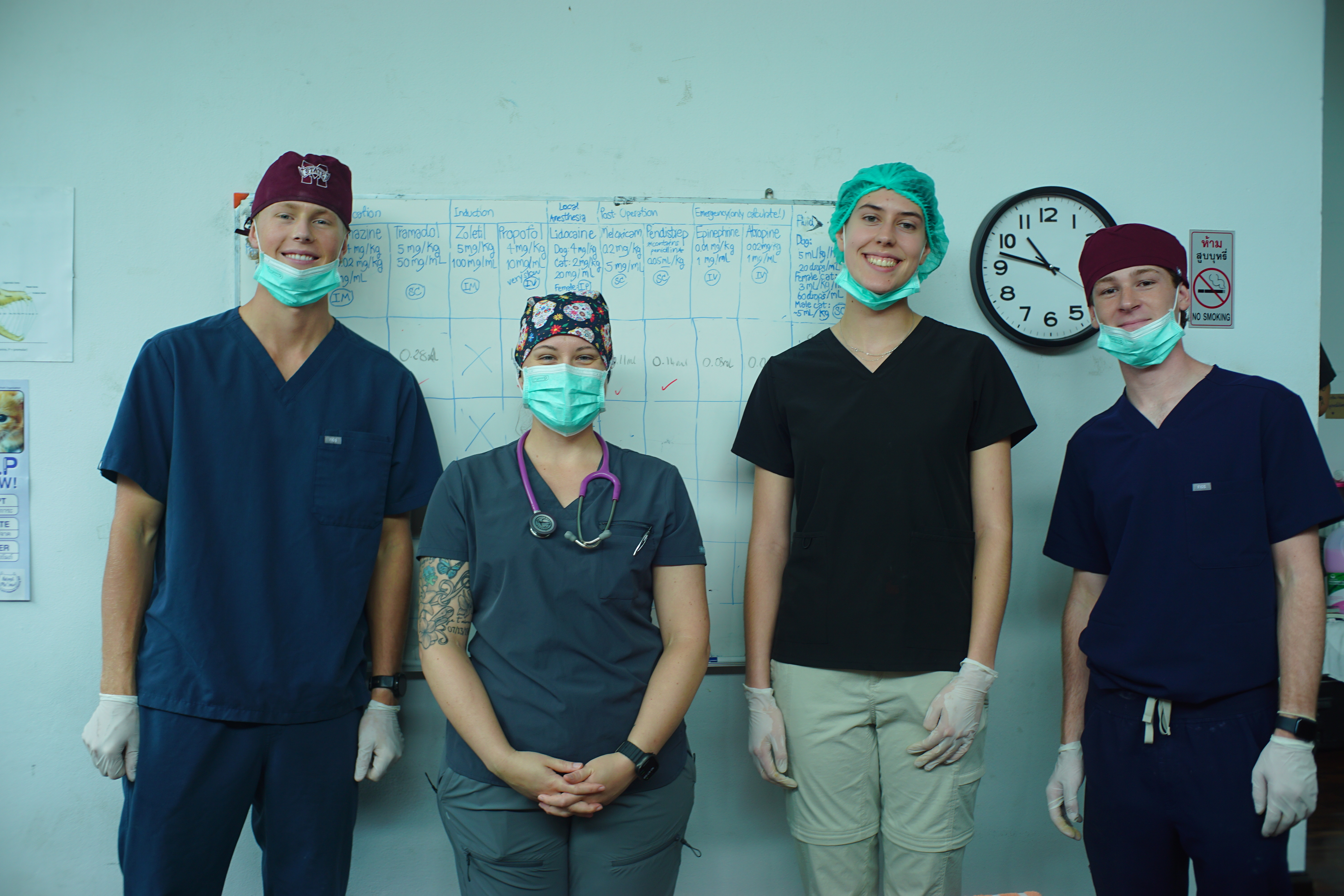 Four college students wearing scrubs and masks pose in a clinic in Thailand.