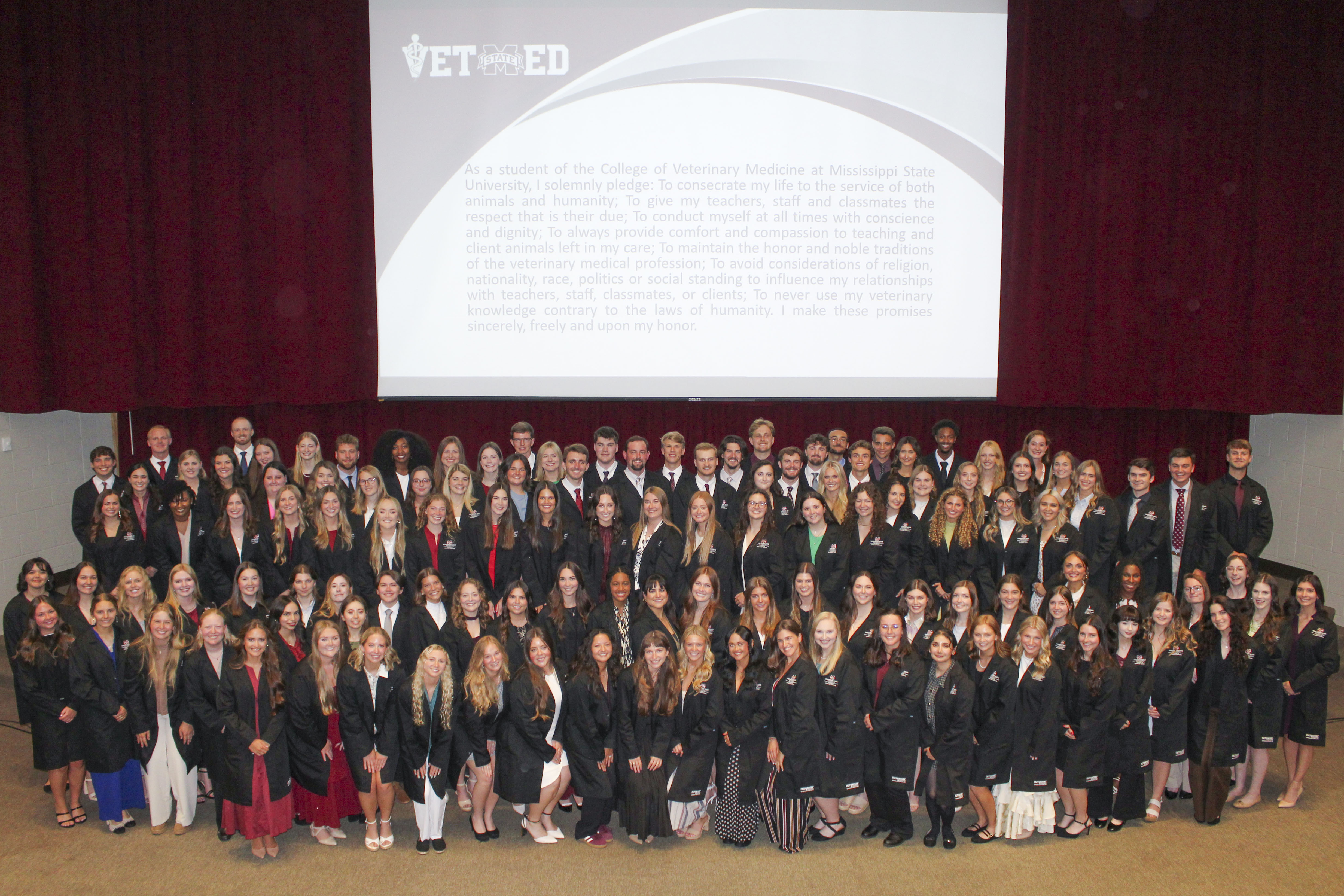 119 members of the Mississippi State University College of Veterinary Medicine DVM Class of 2030 gather onstage for a picture in their new black coats following their Coating Ceremony.