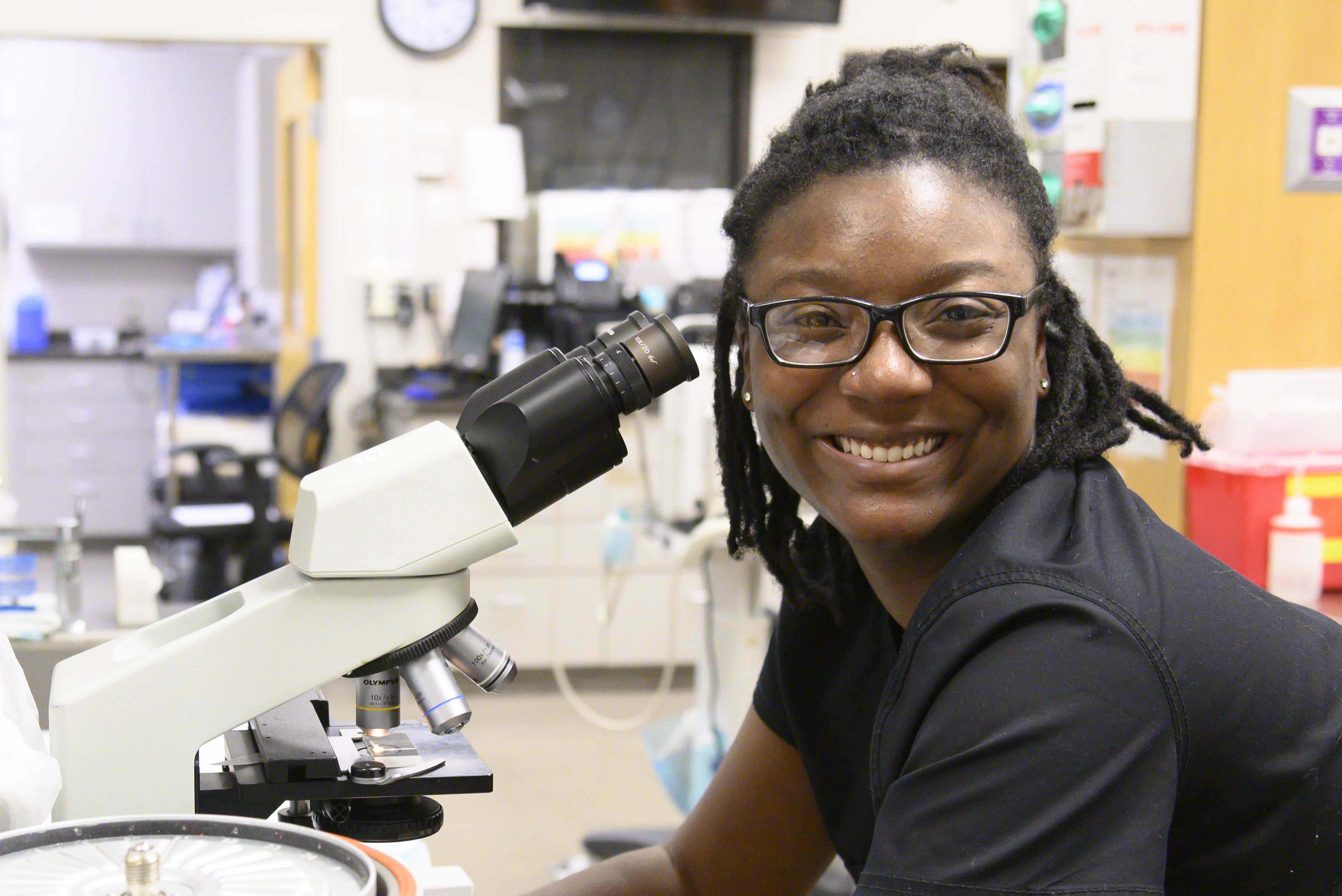 A vet tech smiles from her microscope