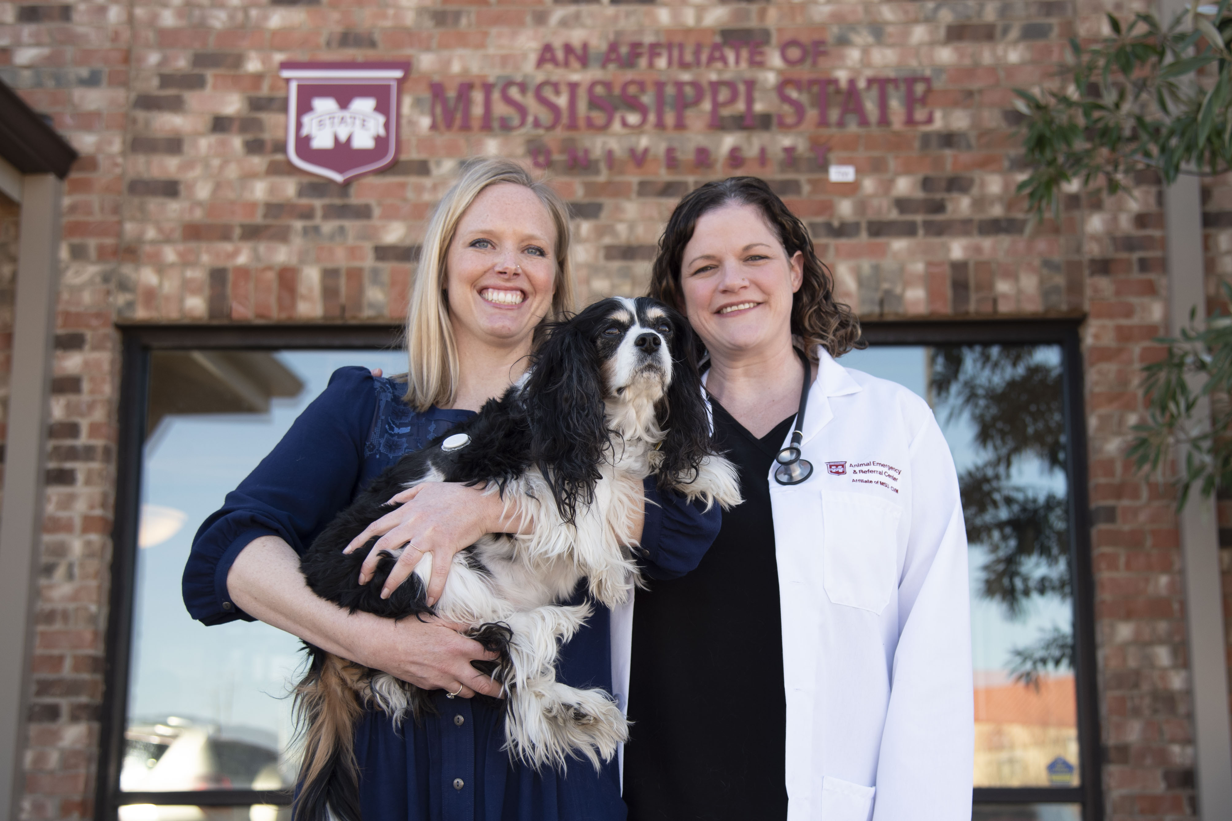 A doctor, client, and patient pose outside of a veterinary clinic
