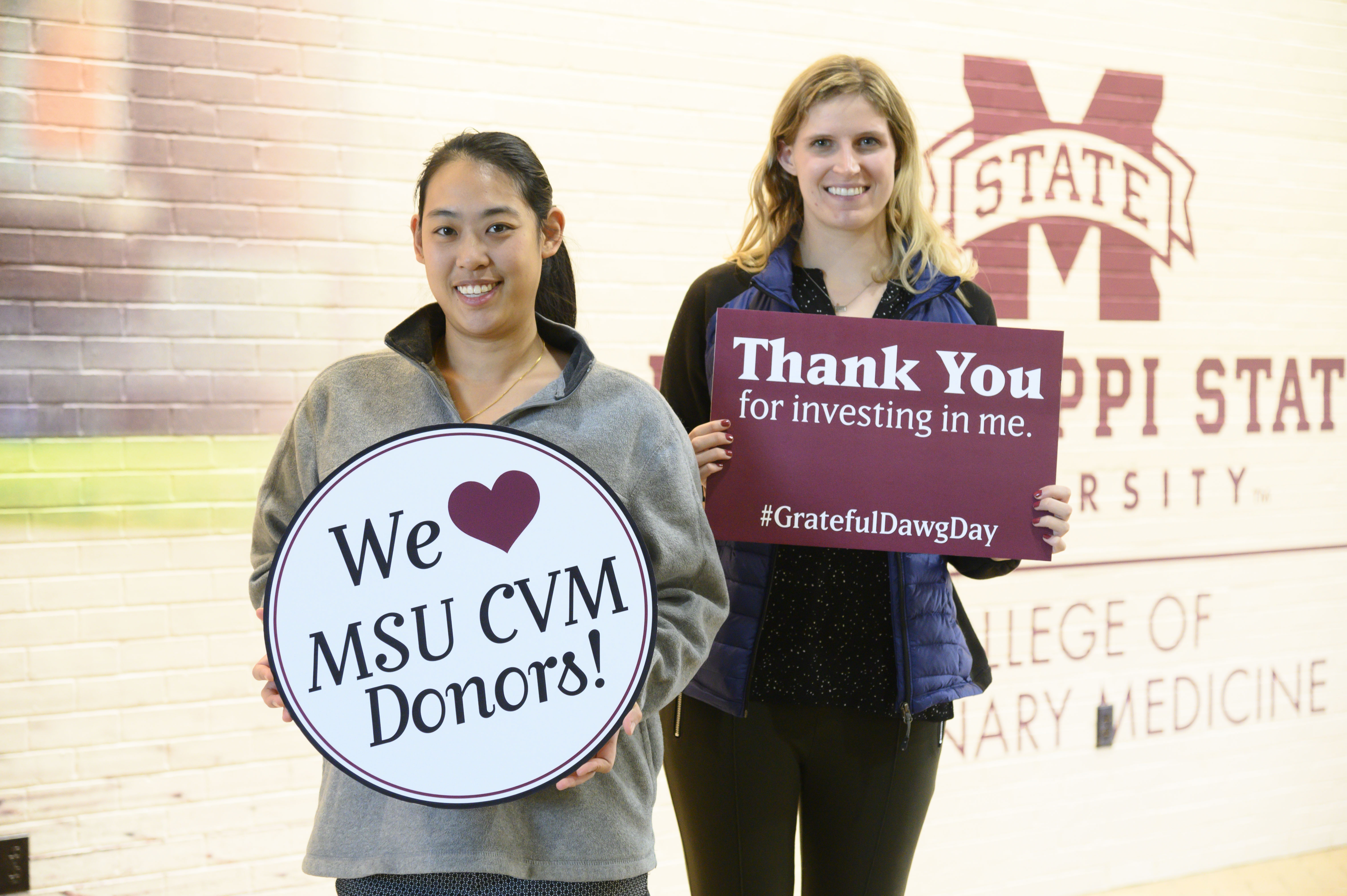 Two female students pose with "thank you" signs